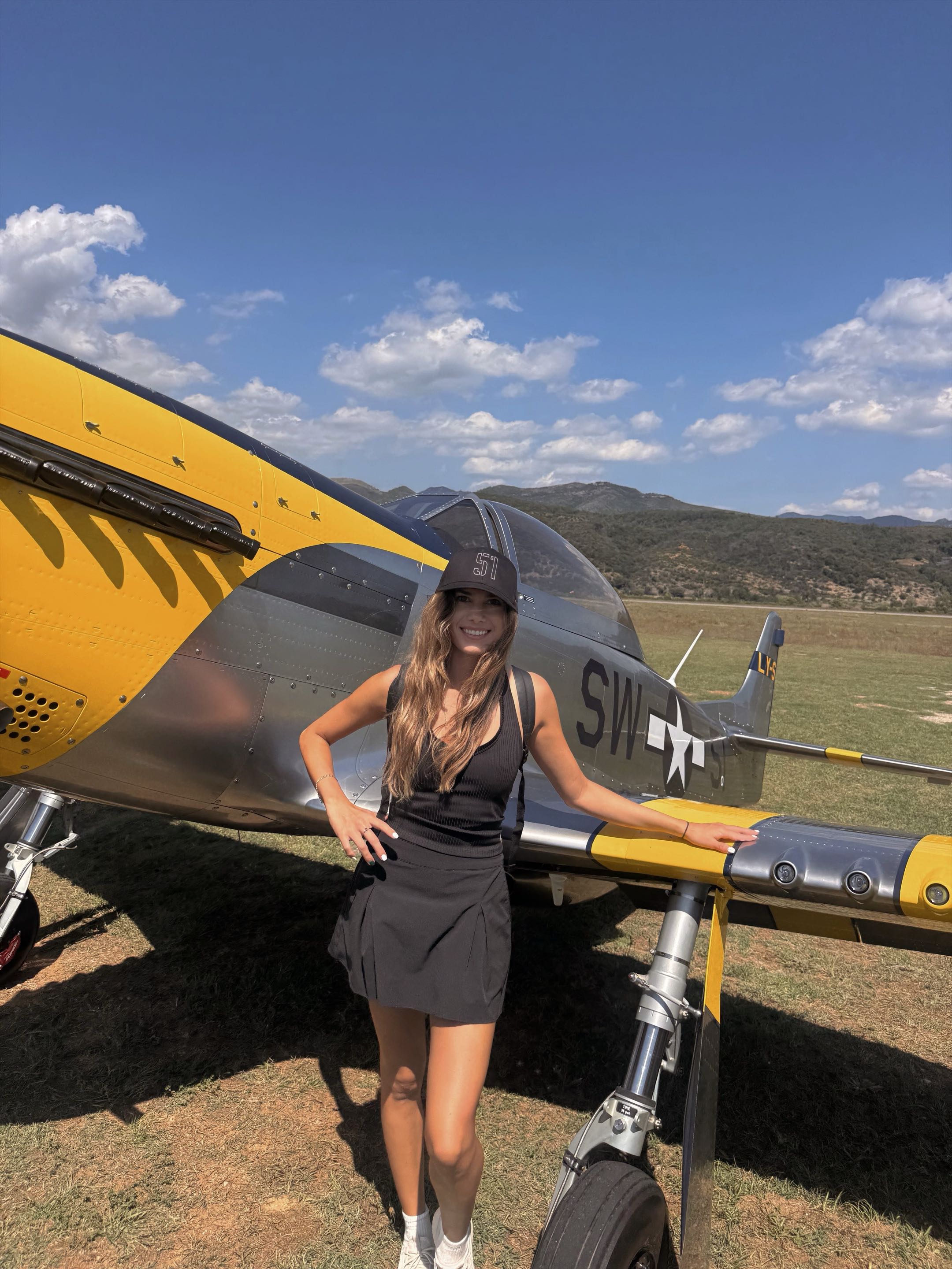 Mikayla beside a P-51 Mustang on a grass strip